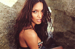a woman with long hair is sitting on a rock looking at the camera