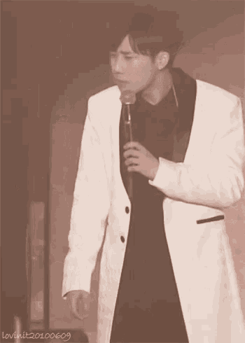 a man in a white suit is holding a microphone in his hand .