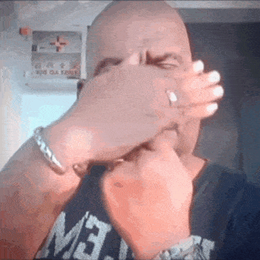 a bald man covering his face with his hands wearing a shirt that says mb on it