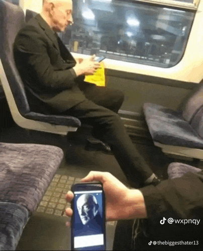 a man in a suit sits on a train looking at his cell phone