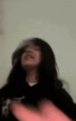 a woman is standing in front of a white wall and making a funny face with her hands .