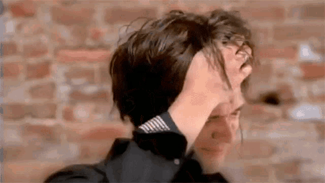 a man is holding his hair in front of a brick wall and making a funny face .
