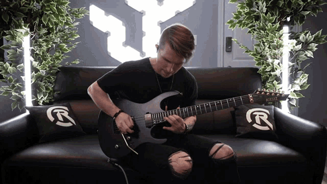 a man is playing a guitar on a couch with pillows that say r on them