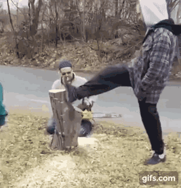 a man is kicking a tree stump in the air while another man watches .