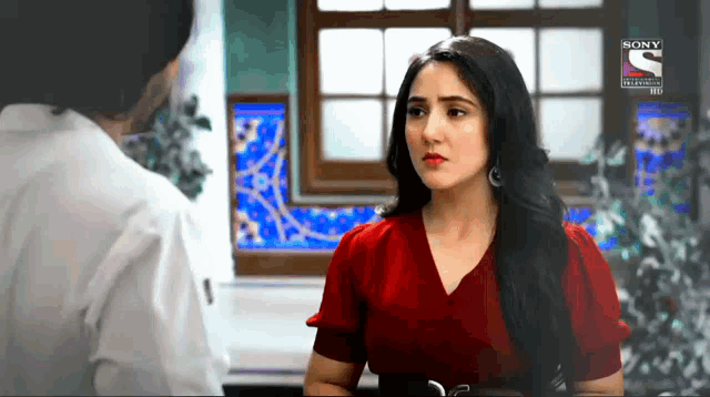 a woman in a red dress is talking to a man in a white shirt in front of a window that says sony
