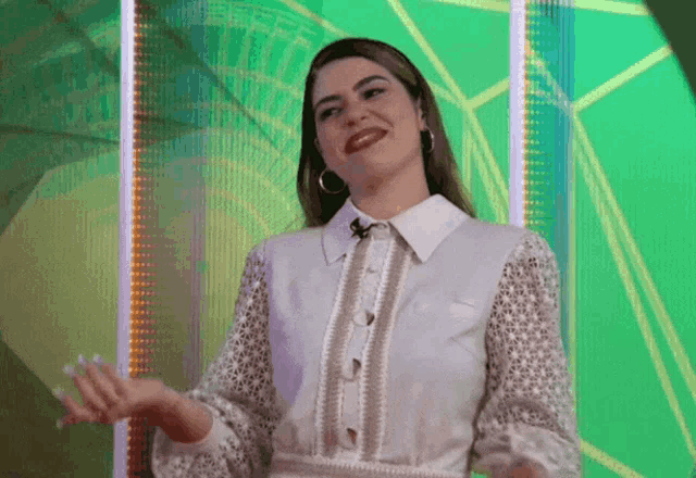 a woman in a white lace shirt is standing in front of a green background .