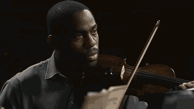 a man in a grey shirt is playing a violin