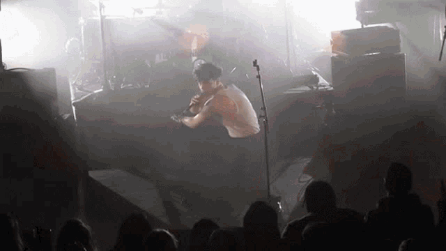 a man is singing into a microphone on stage while a crowd watches .