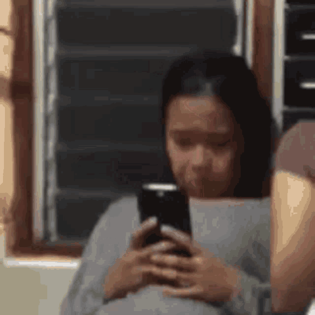 a woman is sitting in front of a window looking at her cell phone .