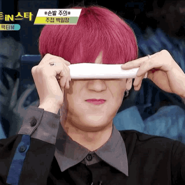 a man with pink hair is covering his eyes with a white cloth