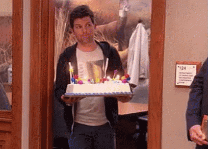 a man is carrying a birthday cake with candles on it .