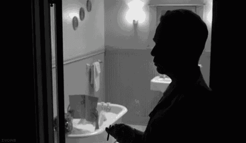 a black and white photo of a man standing in a bathroom .