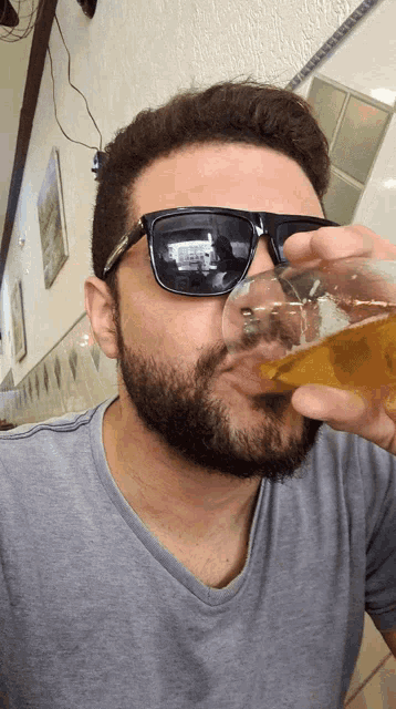 a man with a beard wearing sunglasses is drinking from a glass