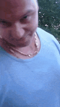 a man wearing a blue shirt and a gold chain around his neck is making a funny face .