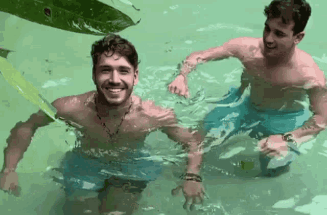 two shirtless men are swimming in a pool and smiling for the camera