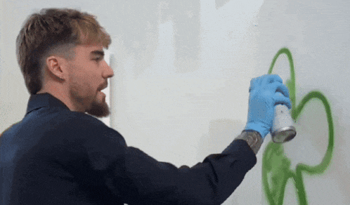 a man wearing blue gloves spray paints a clover on a wall