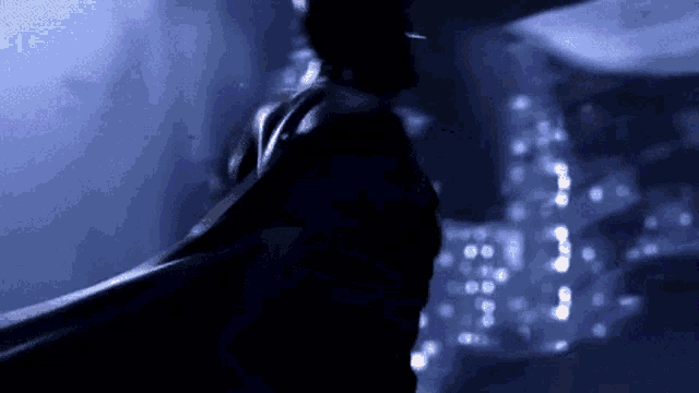 a man in a cape is standing in the dark with a city in the background
