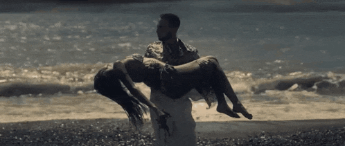 a man is carrying a woman in his arms on a beach .