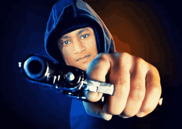 a man in a hoodie holds a gun in front of his face