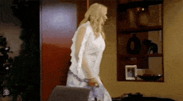 a woman in a white top is standing in front of a shelf with a picture on it
