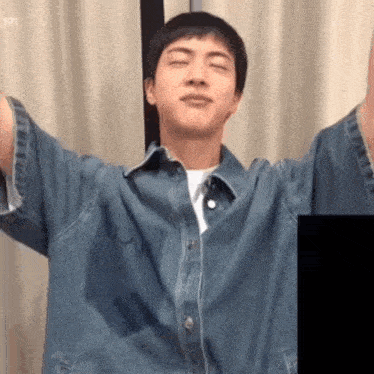 a young man in a denim shirt is standing with his arms outstretched and his eyes closed .