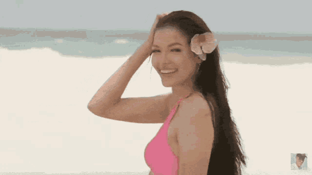 a woman in a pink bikini with a flower in her hair smiles