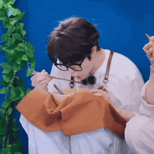 a person wearing glasses is eating a bowl of soup with chopsticks