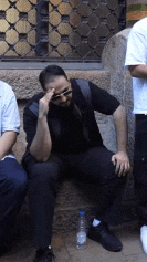 a man sitting on a stone wall with his hand on his forehead