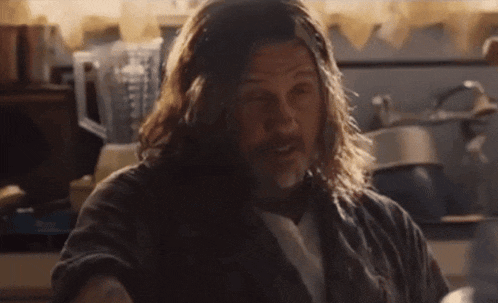a man with long hair and a beard stands in a kitchen