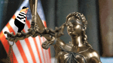 a statue of a blindfolded lady justice stands in front of a flag