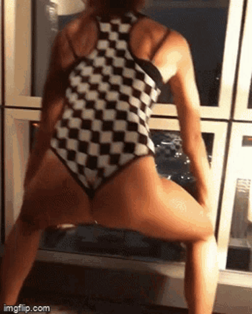 a woman in a black and white checkered bodysuit is dancing in front of a refrigerator