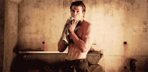 a shirtless man wipes his face with a towel in a bathroom
