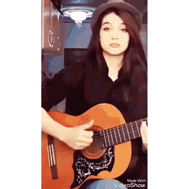 a young girl is playing an acoustic guitar in a kitchen .