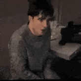 a man in a gray sweater is sitting on a couch in a dark room .