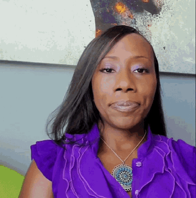 a woman wearing a purple shirt and a necklace looks at the camera