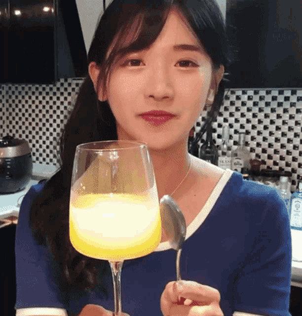 a woman in a blue shirt is holding a wine glass and a spoon