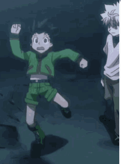 a boy in a green jacket and shorts is jumping in the air while another boy stands behind him .