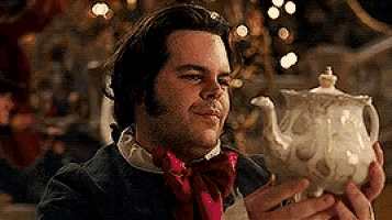 a man in a suit and bow tie is holding a teapot in his hand .