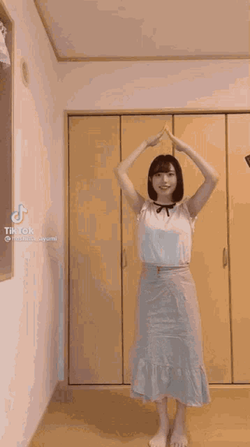 a woman in a white top and blue skirt is dancing in a room with tik tok written on the bottom right corner