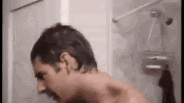 a man without a shirt is taking a shower in a bathroom with a shower head .