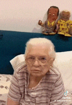 an elderly woman is sitting on a bed with two stuffed animals behind her and a tiktok watermark on the bottom