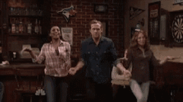 a group of people are dancing in a bar with a dart board in the background .