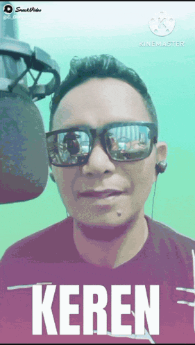 a man wearing sunglasses and ear buds is standing in front of a microphone and says keren