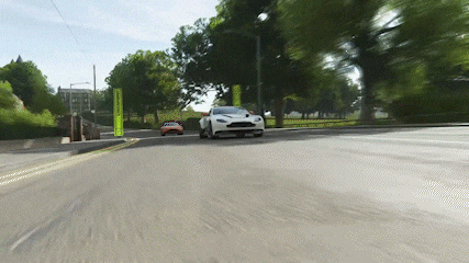 a white sports car is driving down a road next to a park .