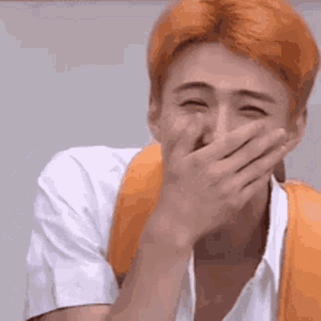 a man with red hair is covering his mouth with his hand and smiling .