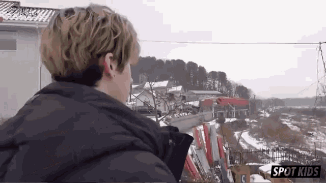 a man in a black jacket is looking out over a snowy landscape with the words spot kids on the bottom right