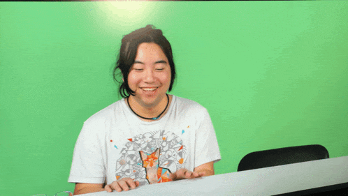 a man wearing a white shirt with a fox on it is sitting in front of a green screen