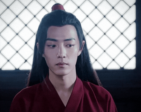 a young man with long black hair is wearing a red kimono and a red top with a red flower in his hair .