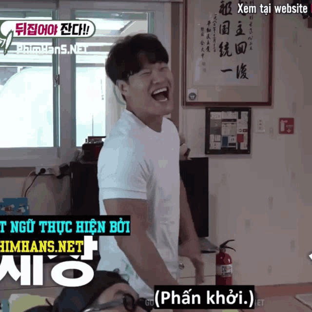 a man in a white shirt is laughing in front of a fire extinguisher in a room