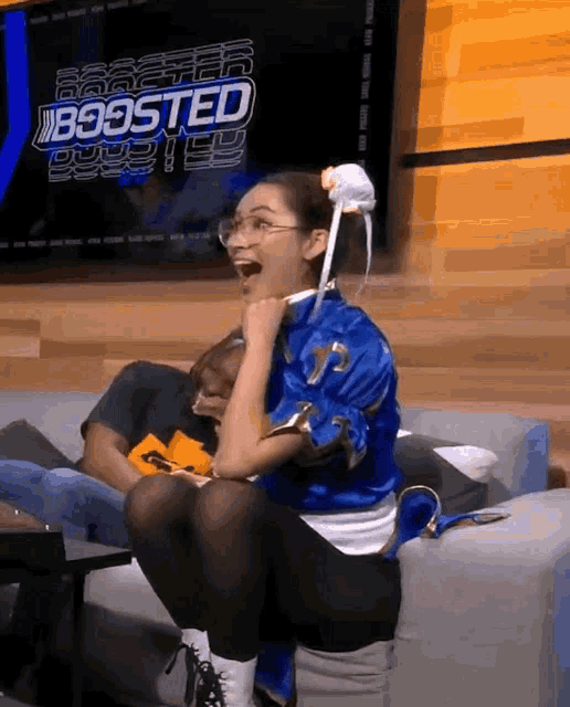 a woman in a chun li costume sits on a couch in front of a screen that says boosted